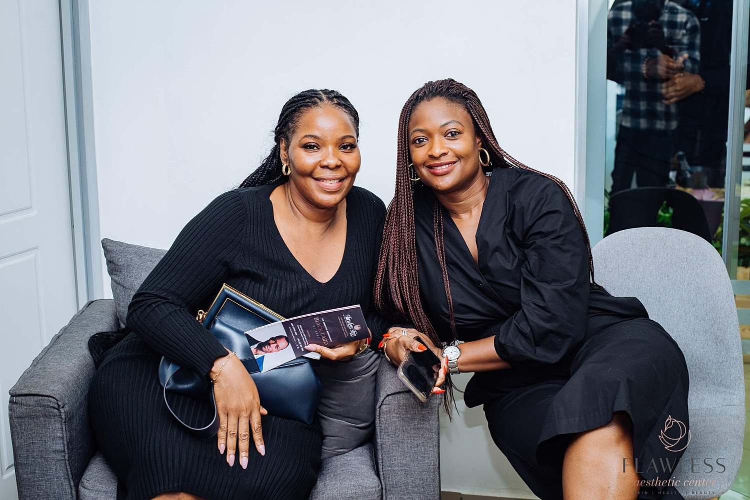 Two smiling women posing together on a sofa.