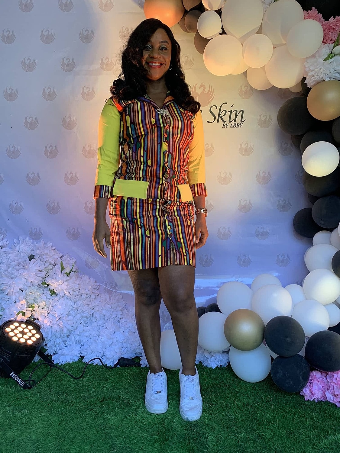 Woman in vibrant striped outfit against balloon backdrop.