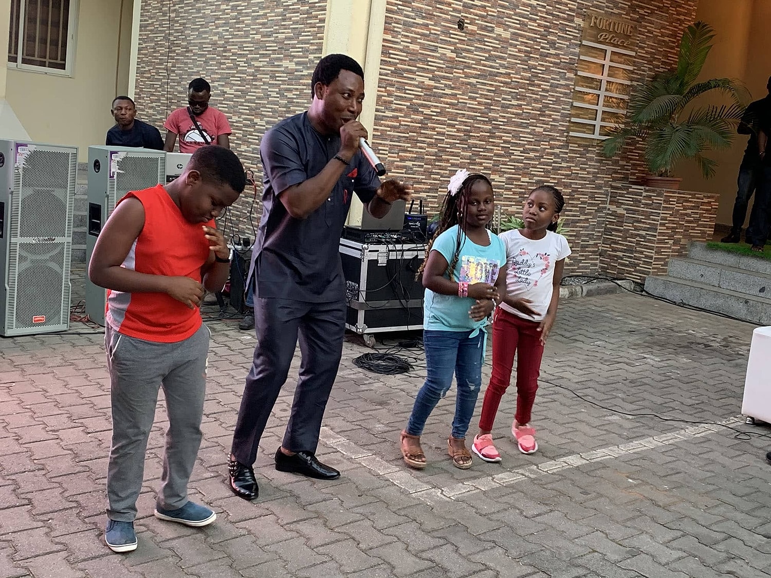 Man singing with children at outdoor event.