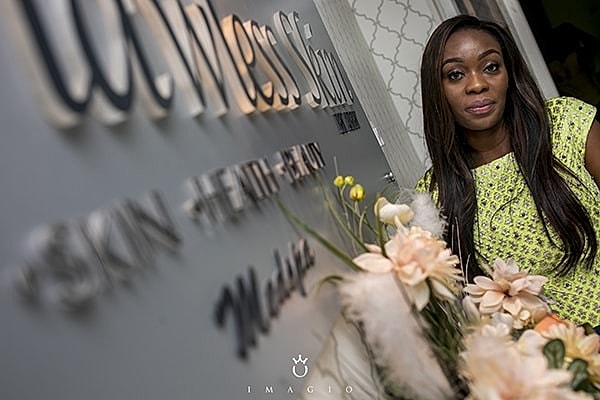 Woman beside wellness studio sign with flowers.