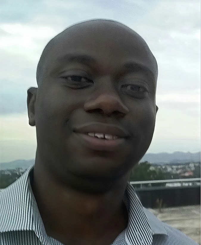 Smiling man outdoors with cloudy background.