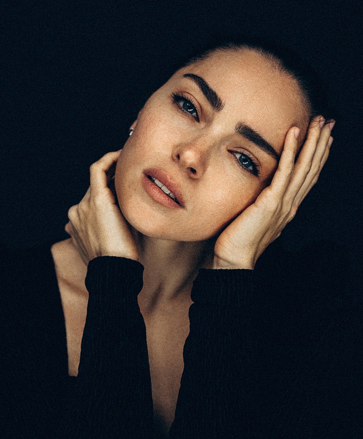 Abuja Facial Treatments model with hands on face, dramatic lighting.