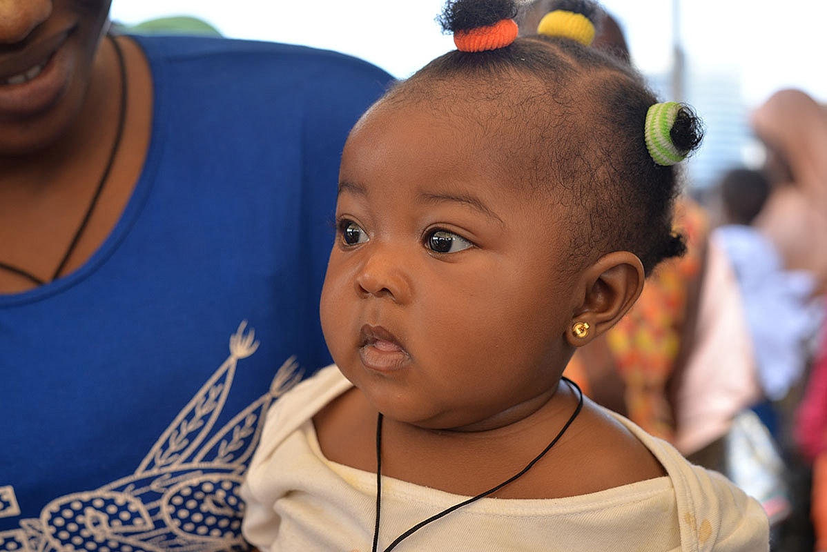 Baby with colorful hair accessories and thoughtful expression.