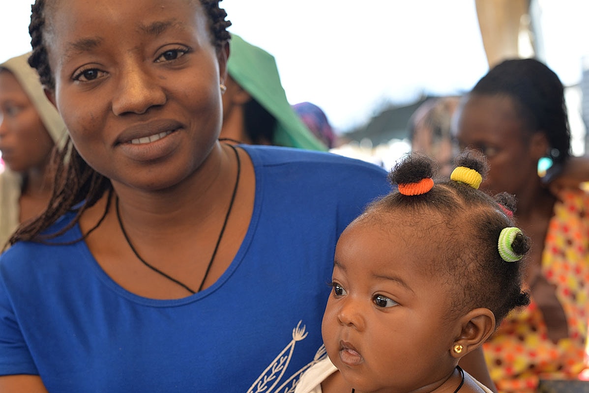 Mother holding baby in a crowded space.