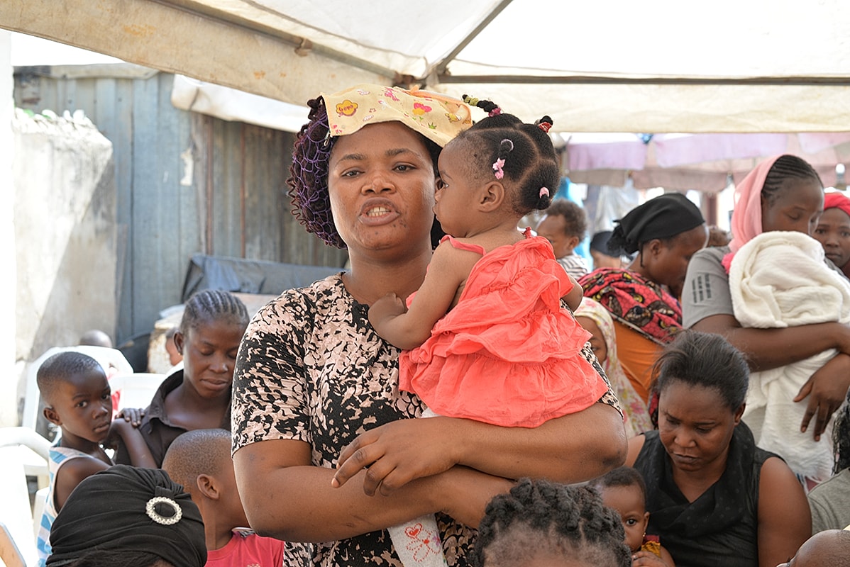 Mother holding child in a crowded setting.