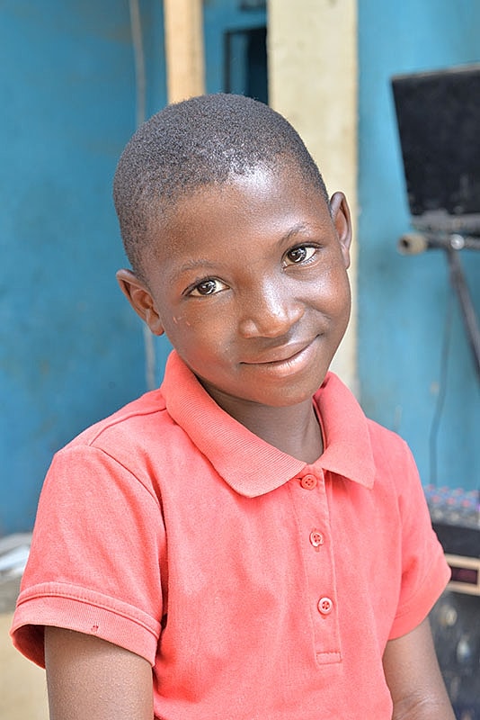 Smiling child in a red shirt, indoor setting.
