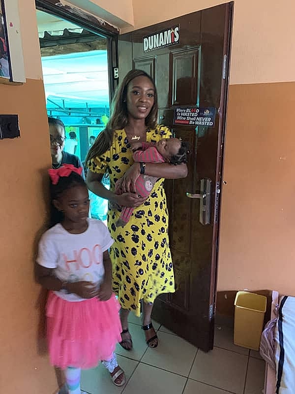 Woman holding baby with two children nearby.