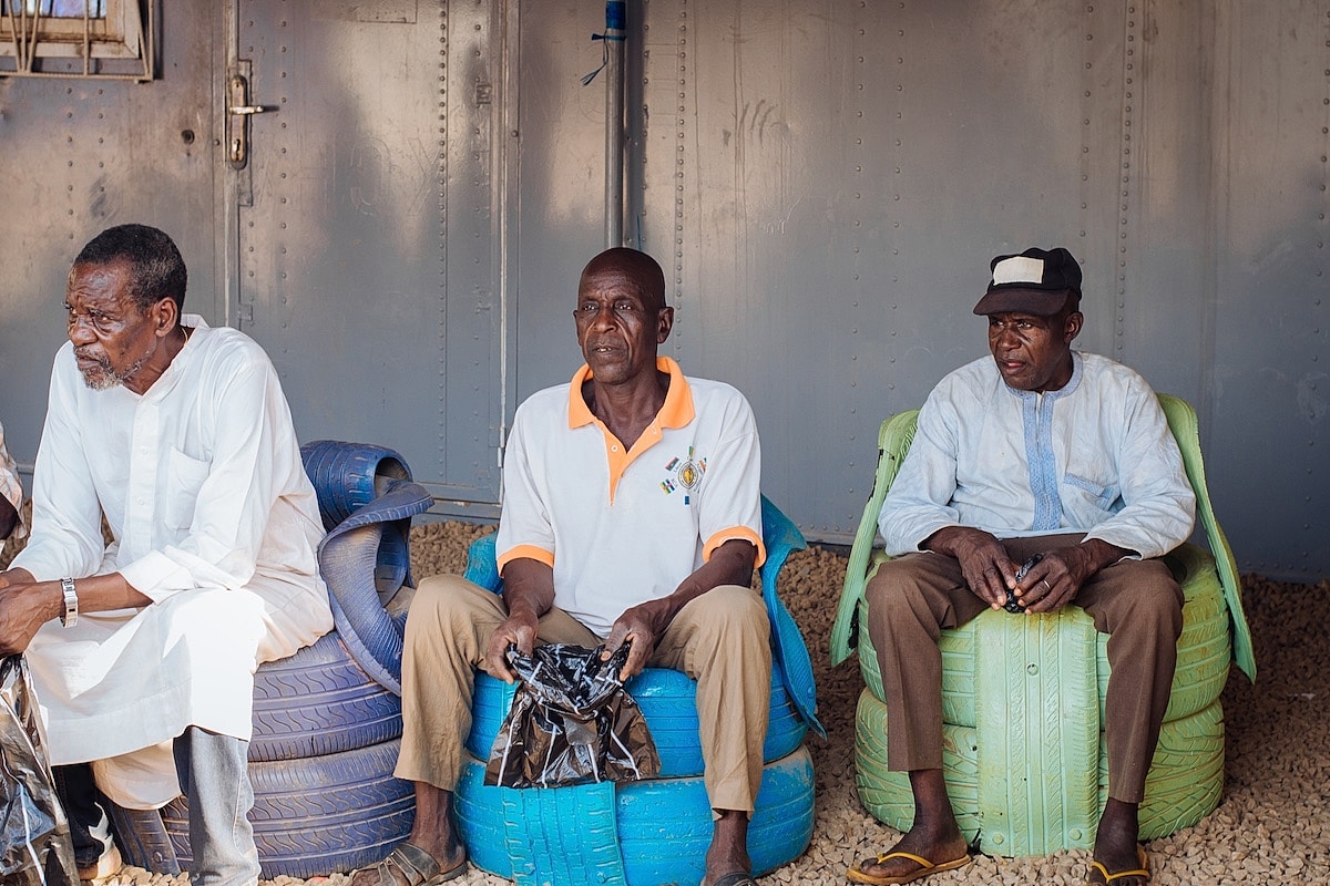 Three men sitting on colorful chairs outdoors.