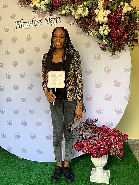 Woman holding sign at floral backdrop event.