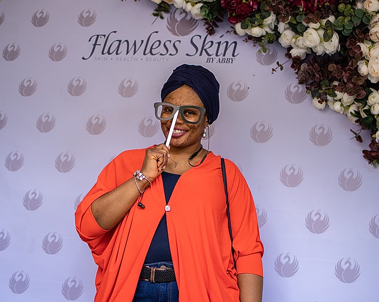 Smiling woman in orange outfit against floral backdrop.