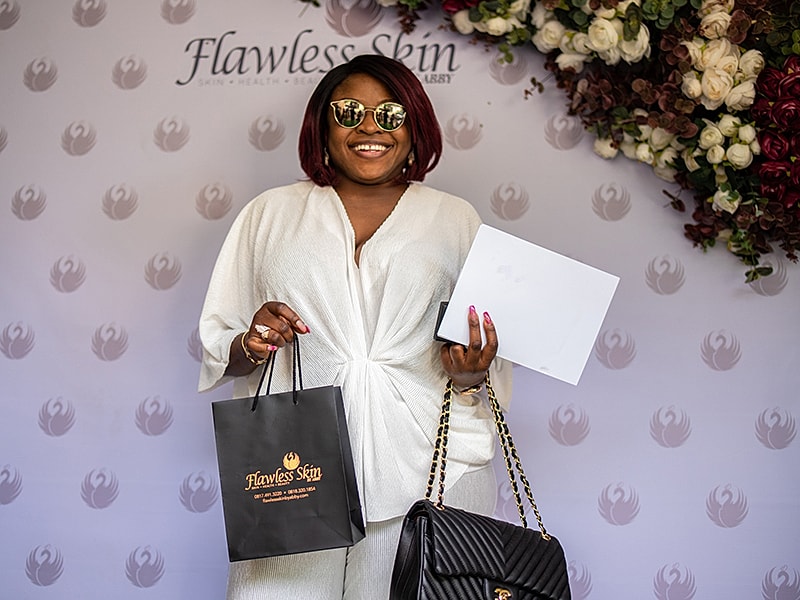 Woman smiling, holding bags, at Flawless Skin event.