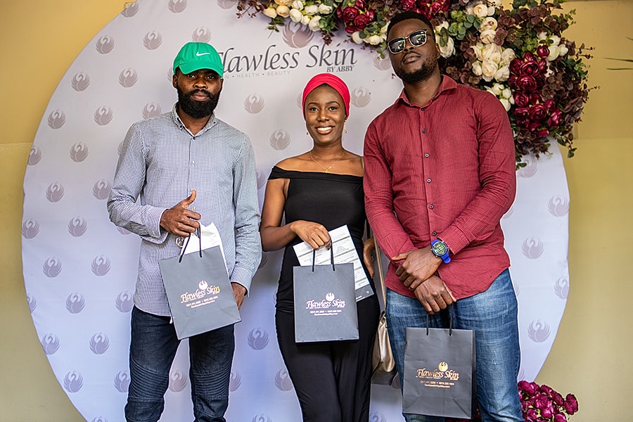 People posing at Flawless Skin event backdrop.