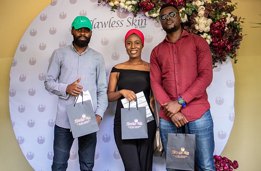 Three people posing with gift bags at event.